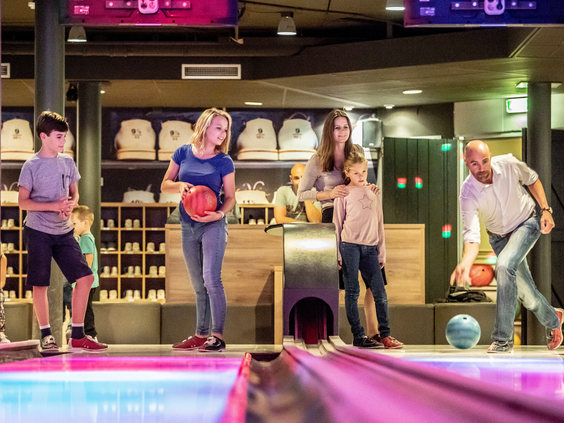 Een gezin is aan het bowlen op een moderne bowlingbaan met gekleurde verlichting op vakantiepark Landal Stroombroek.