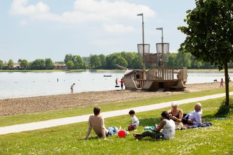 Gasten zonnen op de ligweide aan de recreatieplas, met op de achtergrond een groot houten piratenschip als speeltoestel.