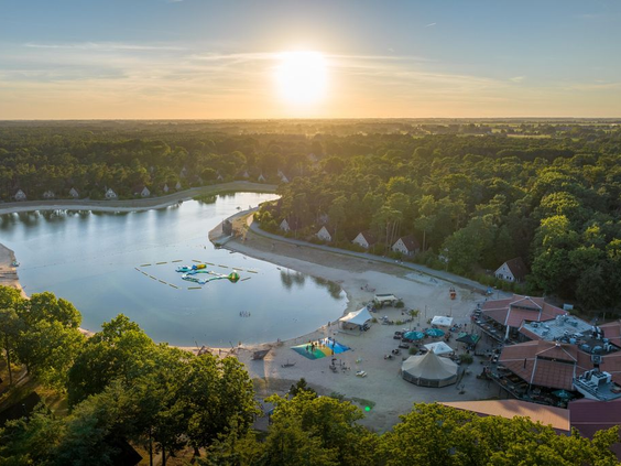 Luchtfoto van Landal 't Loo op de Veluwe met de grote recreatieplas, het strand en de omliggende bossen tijdens zonsondergang.