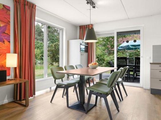 De moderne en sfeervolle woonkamer van een bungalow op Landal 't Loo met een eettafel en uitzicht op de groene tuin en het terras.