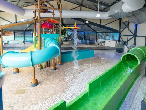 Het overdekte zwembad van Landal 't Loo met een groene glijbaan, een brede familieglijbaan en diverse waterspeeltoestellen.
