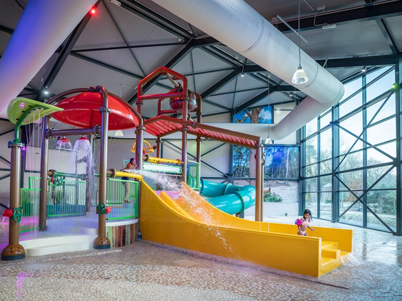 Het kleurrijke peuter- en kinderbad in het binnenzwembad van Landal 't Loo, met een brede gele glijbaan en een waterspeeltuin.