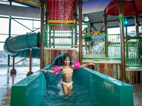 Een lachend meisje glijdt van de waterglijbaan in het zwembad, terwijl een grote emmer met water boven haar omkiept.