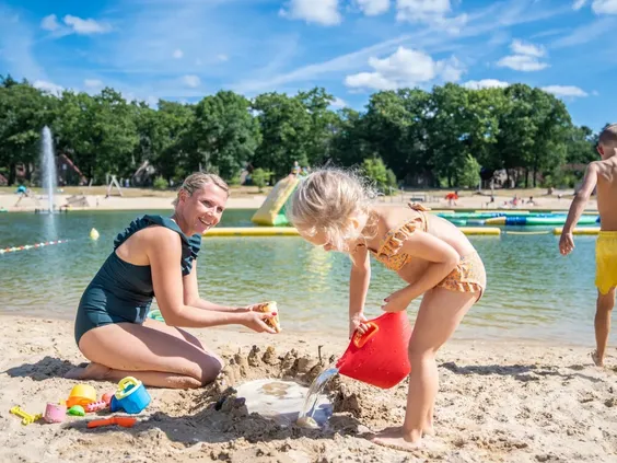Een moeder en haar dochter bouwen een zandkasteel op het strand aan de rand van de recreatieplas op Landal 't Loo.