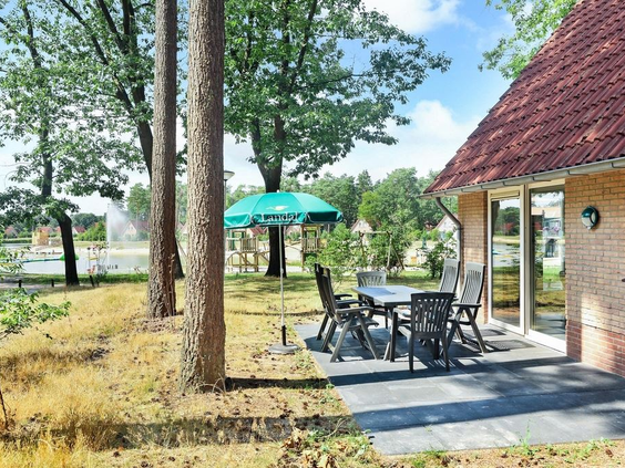 Het zonnige terras van een vakantiehuisje op Landal 't Loo, gelegen tussen de bomen en met uitzicht op het water van de recreatieplas.