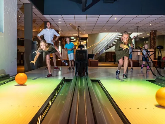 Een enthousiaste familie gooit een bal op de kleurrijke bowlingbaan van Landal 't Loo, een leuke activiteit voor het hele gezin.