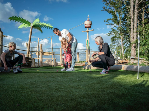 Een gezin met twee kinderen speelt samen adventure golf op een gethematiseerde midgetgolfbaan bij Landal Travemünde.
