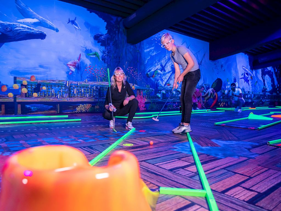 Mensen spelen midgetgolf op een glow-in-the-dark blacklight baan met lichtgevende banen en een onderwaterthema.