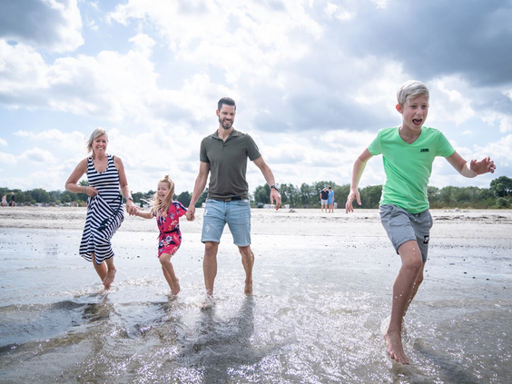 Een vrolijk gezin met een vader, moeder, zoon en dochter rent hand in hand door de branding van de Oostzee.