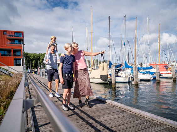Een gezin wandelt langs de pier van de jachthaven bij Landal Travemünde, terwijl de moeder naar de vele zeilboten wijst.
