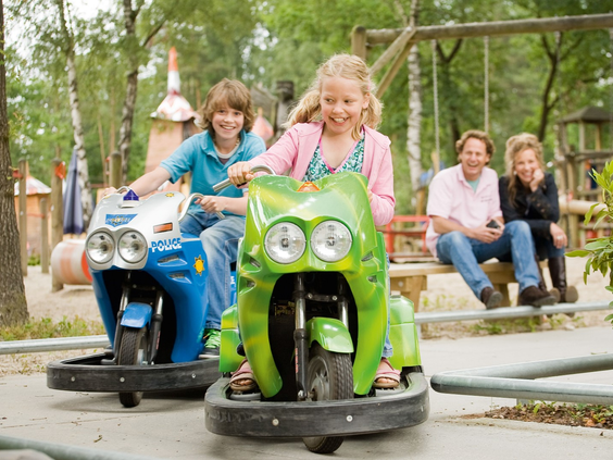 Kinderen rijden op een groene en blauwe scooter op het verkeersplein van Landal Twenhaarsveld, terwijl de ouders toekijken.