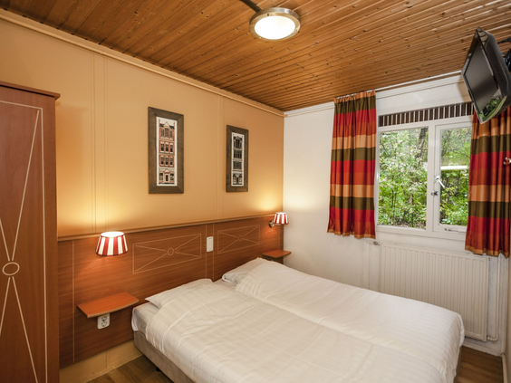 De nette slaapkamer van een bungalow op Landal Twenhaarsveld, met een opgemaakt tweepersoonsbed en uitzicht op het bos.