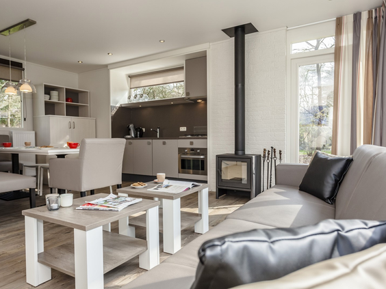 De lichte, modern ingerichte woonkamer van een bungalow op Landal Twenhaarsveld, met een zithoek en een houtkachel.