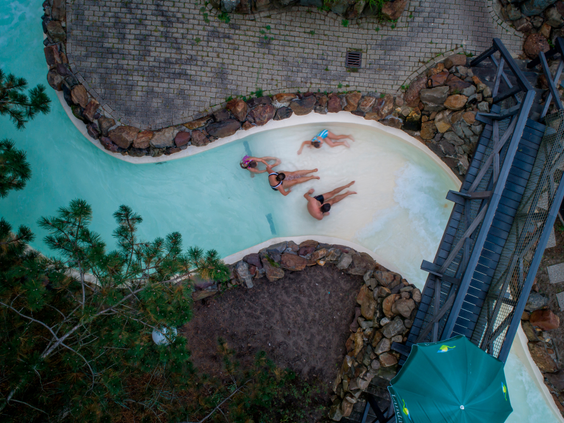 Gasten drijven in de wildwaterbaan die door de natuur slingert, van bovenaf gezien, bij het subtropisch zwemparadijs van Landal Vennenbos.