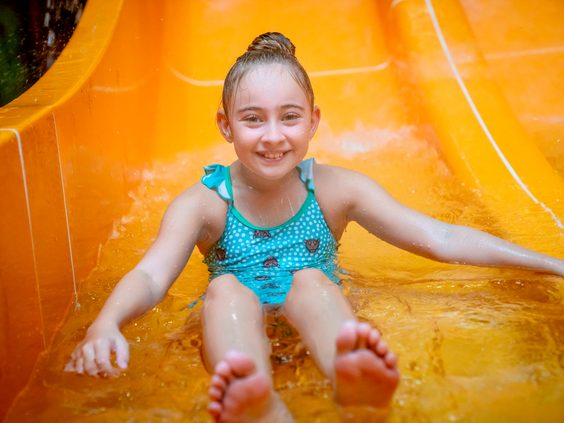 Lachend meisje glijdt van de snelle gele waterglijbaan in het subtropische zwemparadijs van het kindvriendelijke vakantiepark Landal Vennenbos.