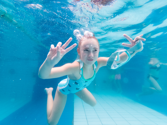 Meisje zwemt en zwaait onder water in het heldere water van het subtropische zwembad op vakantiepark Landal Vennenbos.