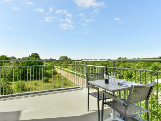 Het balkon van een appartement op Landal Vitamaris met een zitje en een prachtig uitzicht over de groene duinen van Schiermonnikoog.