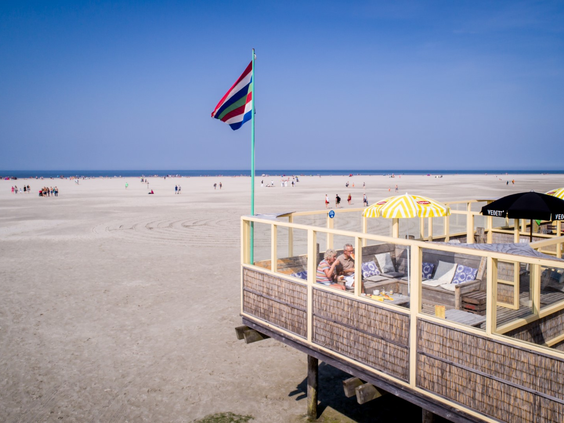 Strandpaviljoen De Marlijn op het brede, zonnige strand van Schiermonnikoog, met een wapperende Schiermonnikoog-vlag.