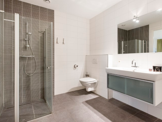 De ruime en moderne badkamer van een appartement op Landal Vitamaris, voorzien van een inloopdouche, toilet en wastafel.