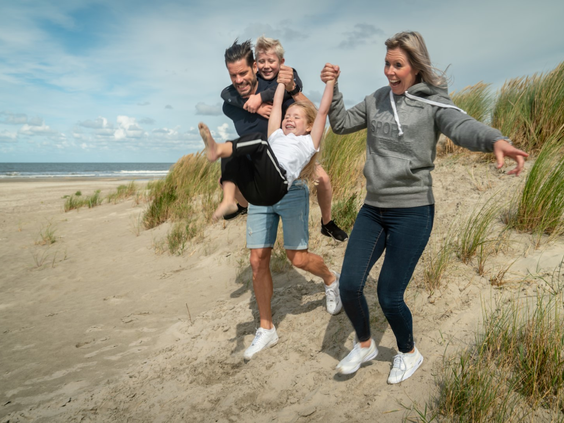 Een vrolijk gezin met twee kinderen rent lachend hand in hand van een duin af op het eiland Schiermonnikoog.