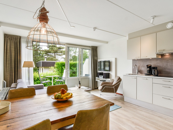 Het moderne interieur van een appartement op Landal Vitamaris, met een open keuken en een ruime houten eettafel die uitkijkt op het terras.