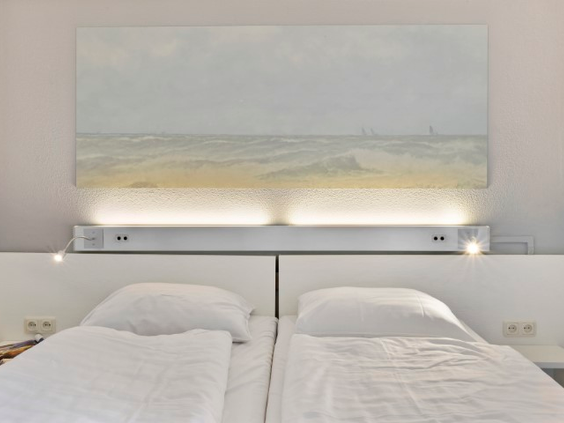 Nette slaapkamer in een appartement van Landal Vitamaris met comfortabele bedden en een schilderij van de zee boven het hoofdeinde.