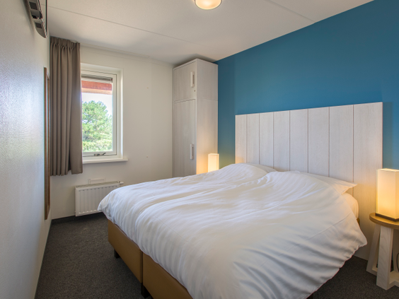 Comfortabele slaapkamer met een opgemaakt tweepersoonsbed en een blauwe muur in een appartement van Landal Vlieduyn.