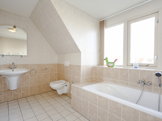 Ruime en lichte badkamer met een comfortabel ligbad, wastafel en toilet in een vakantiewoning op Landal Vogelmient.