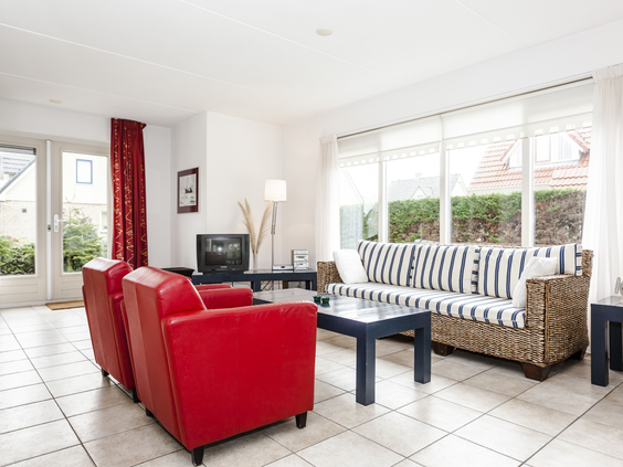Sfeervolle woonkamer in strandstijl met een gestreepte bank, rode fauteuils en tegelvloer in een vakantiehuis op Landal Vogelmient.