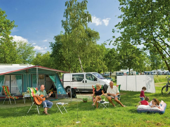 Een familie ontspant op hun ruime kampeerplaats op de camping van Landal Warsberg, met een tent en een kampeerbusje.