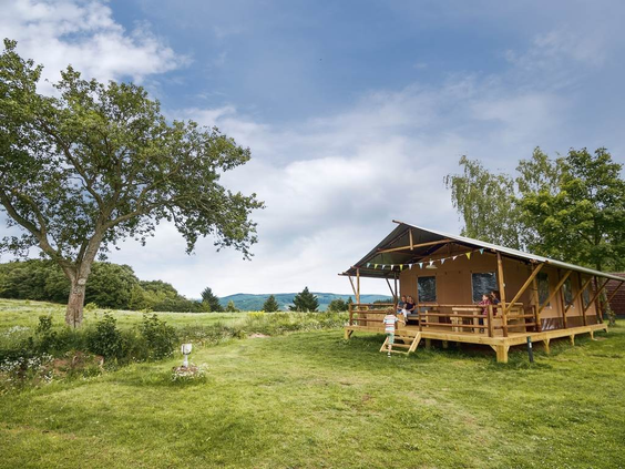 Een luxe en ruime glamping safaritent met een houten veranda op een groot grasveld op de camping van Landal Warsberg.