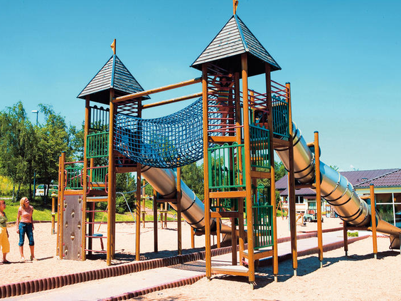 Het grote houten speelkasteel met torens, glijbanen en een klimnet in de buitenspeeltuin van vakantiepark Landal Warsberg.