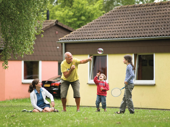 Een familie met opa speelt met bellenblaas op het grasveld bij hun vakantiebungalow op Landal Warsberg.