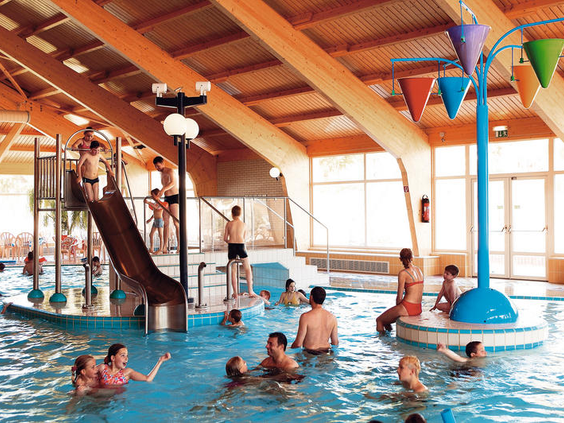Kinderen en volwassenen spelen in het overdekte binnenzwembad met een glijbaan en stroomversnelling op Landal Warsberg.