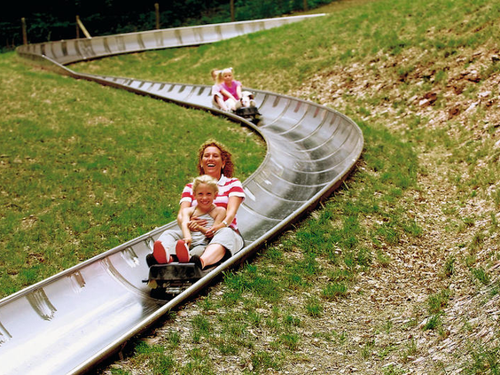 Een moeder en kind roetsjen in een karretje van de zomerrodelbaan (Sommerrodelbahn) in Saarburg, de attractie direct naast Landal Warsberg.