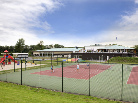De all-weather tennisbaan en sportvelden met een speeltuin op de achtergrond bij het centrumgebouw van Landal Waterparc Veluwemeer.