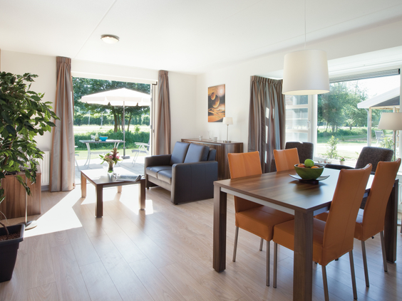 De lichte woonkamer van een vakantiehuis met een eethoek en een zithoek die via openslaande deuren toegang geeft tot de tuin en het terras.