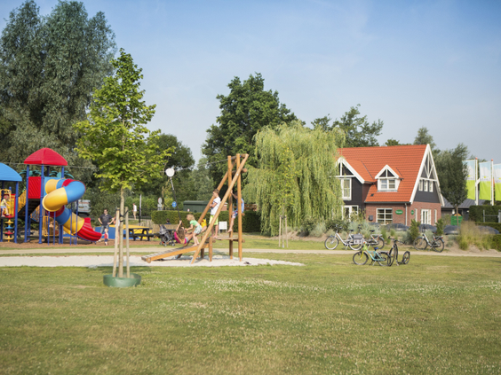 De ruime buitenspeeltuin met een groot grasveld en diverse houten speeltoestellen op Landal Waterparc Veluwemeer.