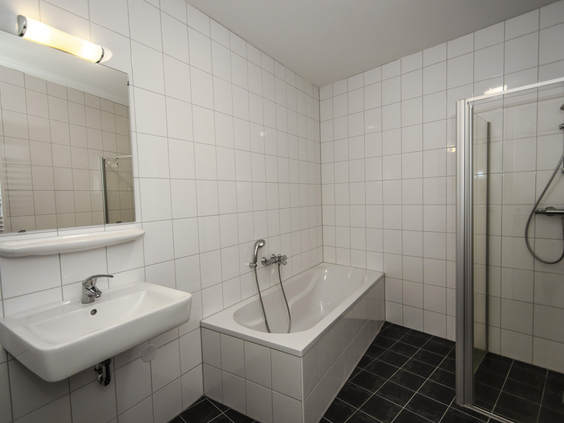 Een nette badkamer met witte tegels, voorzien van een ligbad met douche, wastafel en spiegel in een accommodatie op Landal Waterparc Veluwemeer.