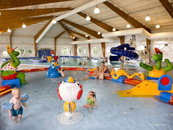 Het overdekte zwembad van Landal Waterparc Veluwemeer met een kleurrijk peuterbad vol speeltoestellen en een glijbaan op de achtergrond.