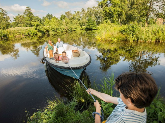 Een jongen trekt een sloep met zijn familie aan boord naar de waterkant in de groene, waterrijke omgeving van Landal Waterresort Blocksyl.