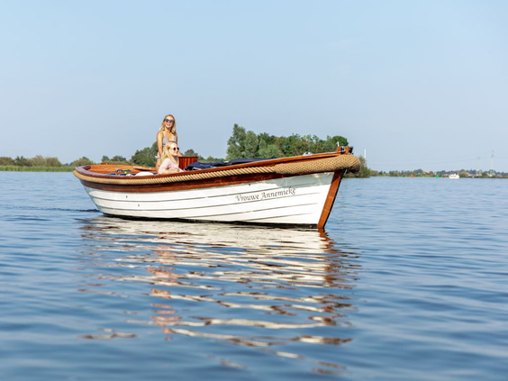 Een vrouw ontspant in een klassieke houten sloep op het water in Nationaal Park Weerribben-Wieden.