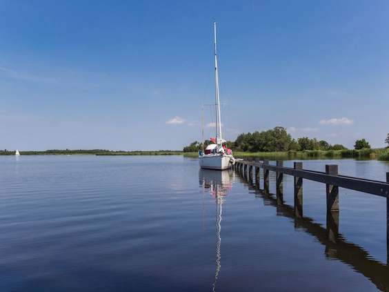 Een zeilboot aangemeerd aan een lange houten steiger op een van de meren in de waterrijke omgeving van Blocksyl, Overijssel.