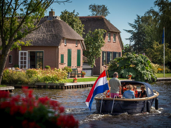Een familie met kinderen vaart in een fluisterbootje met de Nederlandse vlag door een gracht in het pittoreske Giethoorn.