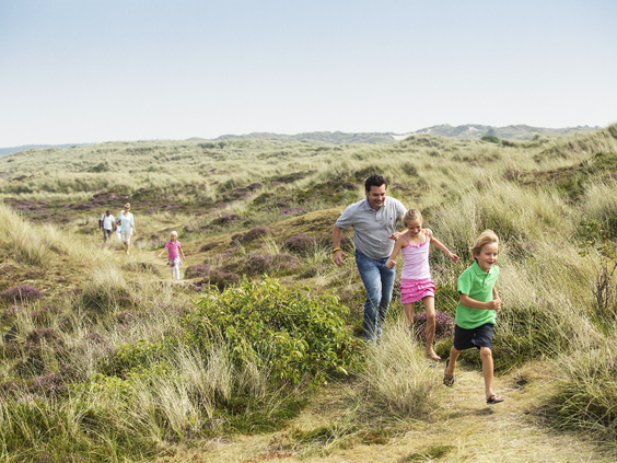 Gezin met kinderen rent en speelt in de duinen op Terschelling, vlakbij Landal West-Terschelling.