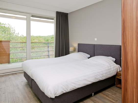 Slaapkamer in een appartement van Landal West-Terschelling met een groot raam dat prachtig uitzicht biedt op de duinen.