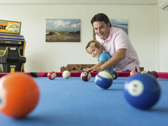 Vader en zoon spelen samen een potje poolbiljart in de recreatieruimte van Landal West-Terschelling.