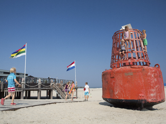 Kinderen spelen op het brede Noordzeestrand van Terschelling bij een grote rode boei.