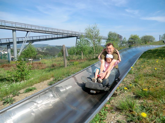 Een vader en dochter roetsjen van de zomerrodelbaan (Sommerrodelbahn) op de Erlebnisberg Kappe, een populaire attractie in de buurt van Landal Winterberg.