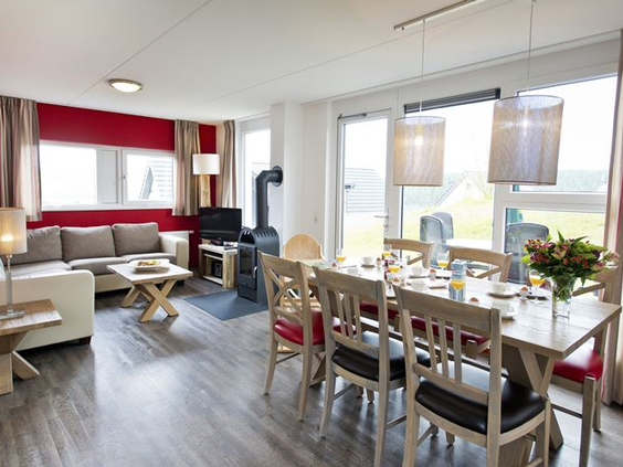De gezellige woonkamer van een vakantiehuis op Landal Winterberg, met een comfortabele zithoek, een houtkachel en een gedekte eettafel.